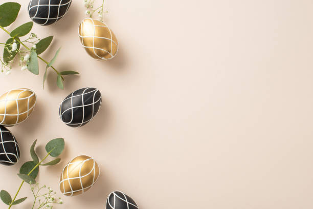 istock Sophisticated Easter setting: top view photo of opulent black and gold eggs, eucalyptus sprigs, gypsophila, positioned on a creamy beige surface, space for inscription 2005516127