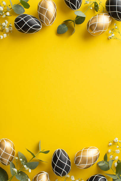 istock Refined Easter setting. Top view vertical shot of deluxe black and gold eggs, natural eucalyptus sprigs, soft gypsophila accents, laid out on lively yellow backdrop with empty space for text or advert 2005516150