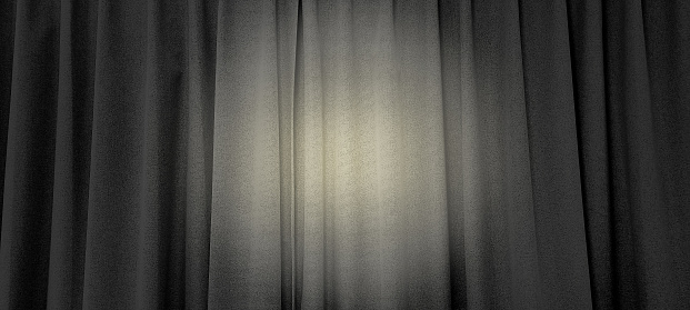 close up view of dark black in thin and thick vertical folds made of black out sackcloth fabric, panoramic view. grey curtain background with yellow spotlight at center in theater or cinema.