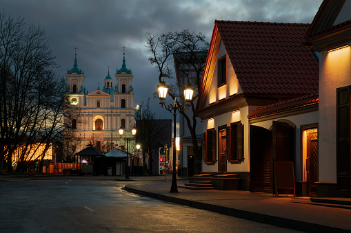 View of the recreated historical buildings on Zamkovaya Street and the Cathedral of St. Francis Xavier in the background at dusk with night lighting, Grodno, Belarus