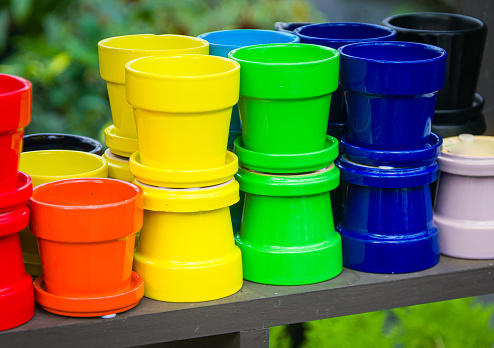 A grouping of small flower pots in a rainbow of colors sit on a wooden shelf.