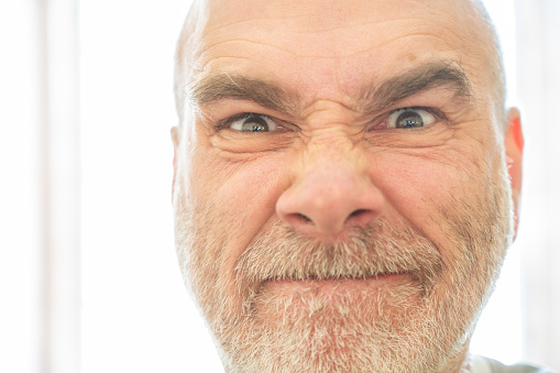 Close-up headshot on angry mature bald man's face with a beard on a white background