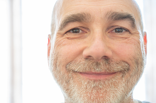 Close-up headshot on smiling mature bald man's face with a beard on a white background