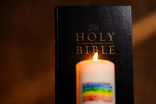 Holy Bible and burning candle with LGBT rainbow flag