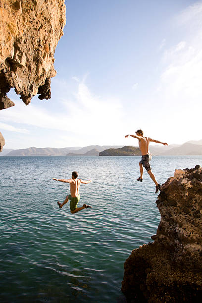 Two young men diving off rock into sea, mid-air, rear view  jumping into water stock pictures, royalty-free photos & images