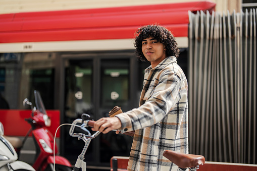 A happy hipster tourist is pushing his rental bike aside while walking on the streets of Barcelona.