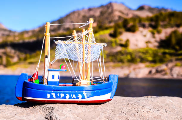 Two blue and yellow plastic toy boats float on a calm water surface. Gentle ripples reflect the sunlight, creating a peaceful and playful scene.