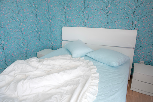 Bedroom interior, cozy bed with light blue and white linen. Pillow and blanket