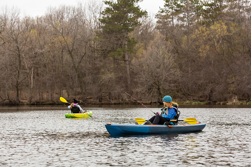 Two girls kayak fishing on a springtime day on the lake.