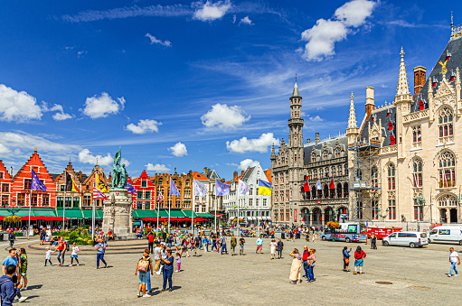 Bruges, Belgium, July 5, 2023: people tourists walking down Markt square with row of colorful Flemish style townhouses houses buildings, Provinciaal Hof, Historium Bruges museum in Brugge old town