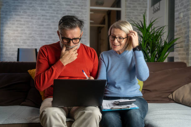 Senior couple sitting at the kitchen table looking at digital tablet and recalculating their expenses.