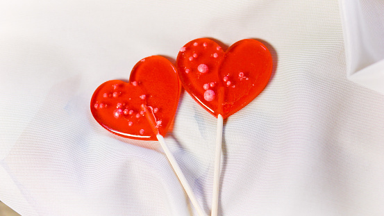 Valentine's Day concept. Two red paired heart-shaped lollipops lying on satin beige white fabric. High quality 4k footage. Close up. Soul mates. Love at first sight. Eternal love.