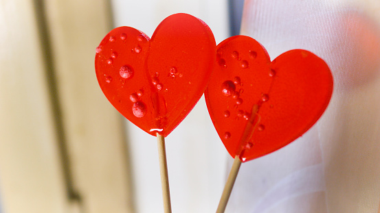 Valentine's Day concept. Two red paired heart-shaped lollipops stuck together against a neutral blurred background. High quality 4k footage. Close up. Soul mates. Love at first sight. Eternal love.