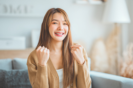 Smiling asian young woman express happy fight to success on sofa at home, cheer up