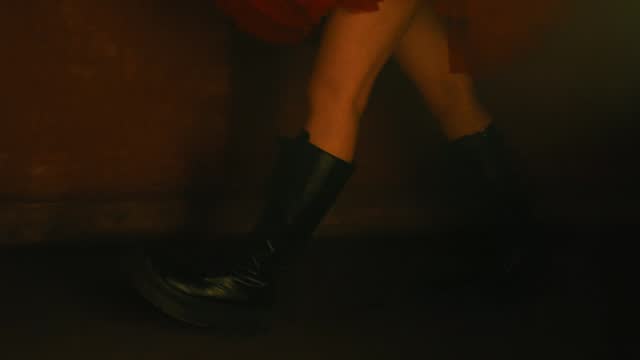 Woman in red skirt and black boots standing in moody lighting.