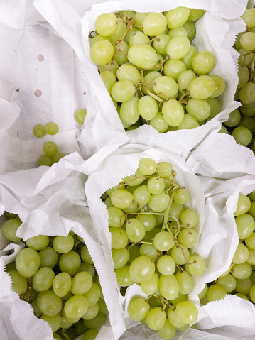 White paper bags with green bunches of grapes in the supermarket.