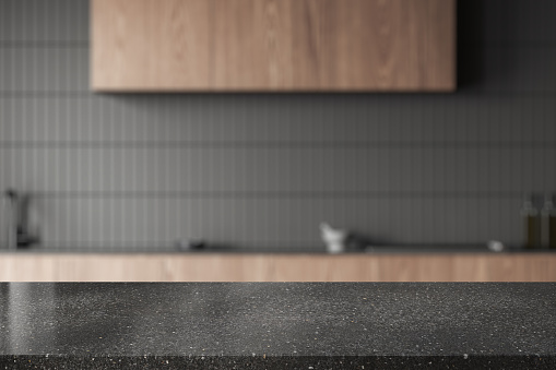 Dark stone product display table standing in stylish blurry kitchen with gray tiled walls and wooden cabinets and cupboards. 3d rendering