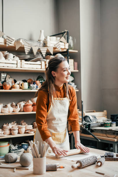 istock Artisan woman in lighted pottery studio, rolling clay for modelling 2005863323