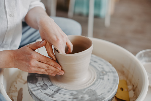 Pulling out the walls of a clay product on a potter's wheel. Hands of a Ceramist creating pottery from white clay. Close-up