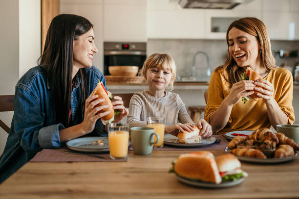 Candid family dialogue Two women and their adopted girl sharing stories over a breakfast gay dinner table stock pictures, royalty-free photos & images