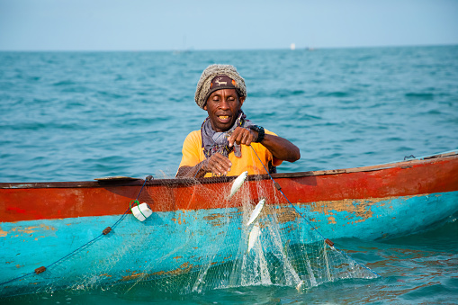 Morondava,Madagascar . 18 october 2023. Malagasy fisherman on homemade wooden old pirogue boat in ocean catches fish with net. selective focus, close-up view from ocean