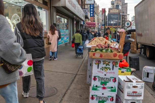 New York, NY, USA 11-09-2023 Produce vendor on busy Chinatown streeet with piles of fruit and vegetable produce scale and shoppers, sweet potatoes and avocados