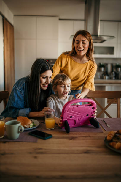 Home learning in progress Two mothers bonding with their adopted child over a meal, as she studies on a tablet gay dinner table stock pictures, royalty-free photos & images