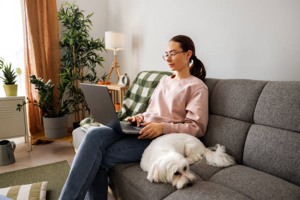 istock Young beautiful female student using laptop while her cute little dog laying next to her 2005885123
