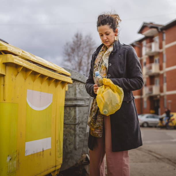 One adult woman stand with plastic waste and yellow bags in front of recycle containers throwing bottle for reuse zero waste eco concept