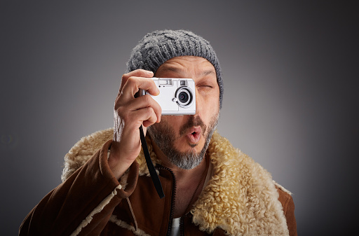 Man wearing leather coat with fur collar and knit hat taking a picture with his old digital camera