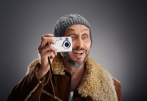 Man wearing leather coat with fur collar and knit hat taking a picture with his old digital camera