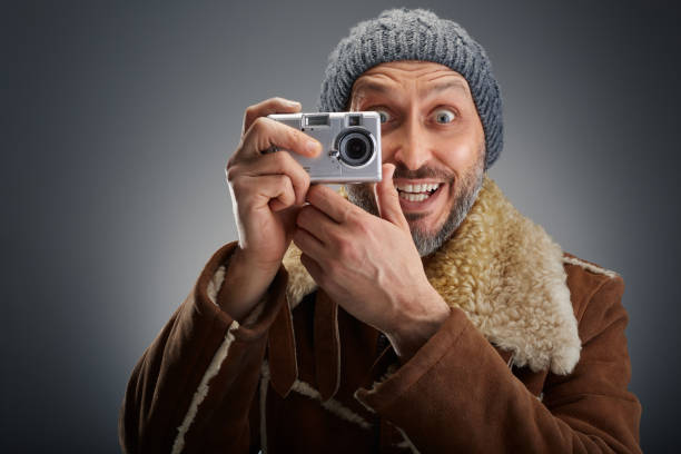 Man wearing leather coat with fur collar and knit hat super is excited while taking a picture with his old digital camera