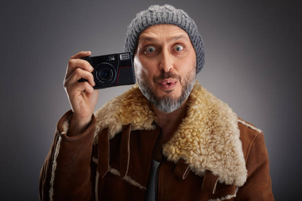 Man wearing leather coat with fur collar and knit hat super is excited while taking a picture with his old digital camera