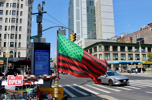 New York, NY USA - August 22, 2023 : Close up of the African American flag waving from a book vendor's table on the corner of 125th Street and Adam Clayton Powell Jr. Boulevard with the historic Hotel Theresa and the Renaissance New York Harlem Hotel in the background on a sunny summer day in Harlem, New York, USA