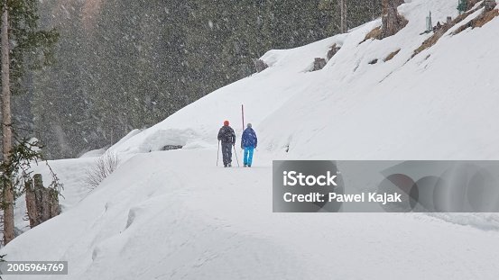 Tourist Couple Passing By Hiking Trail Marker Pole in Austrian Alps During Snow Blizzard on Winter Day