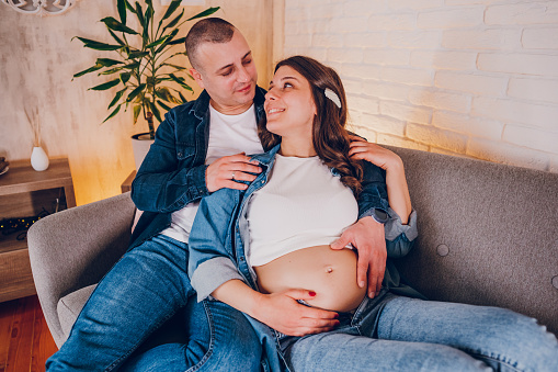 Husband hugs pregnant wife while sitting at home