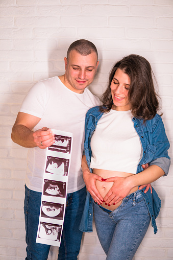 Young Pregnant woman and husband holding ultrasound scan photo and make a heart on her stomach