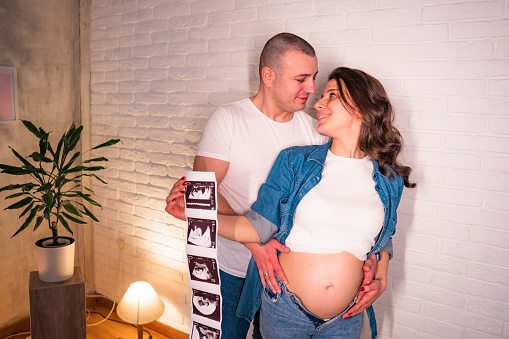 Young Pregnant woman and husband holding ultrasound scan photo and smiling.