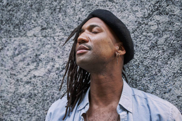 istock handsome African-American man in braids with stylish beret looking away while standing against grey wall and eyes closed 2005988034