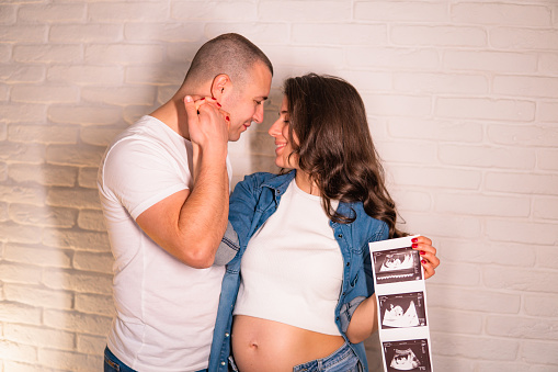Young Pregnant woman and husband holding ultrasound scan photo and smiling.
