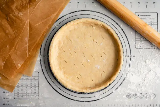 Raw pie crust in a fluted pan on a floured work surface with a French rolling pin and unbleached parchment paper