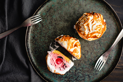 Whole and halved individual servings of bombe Alaska ice cream, cake, and meringue desserts