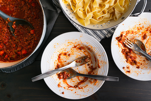 Dirty bowls and silverware with a pot of bolognese sauce and pappardelle in a colander