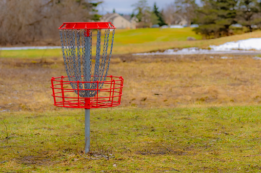 Red disc golf goal, net, pole hole, entrapment basket on a raw winter day.