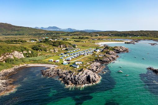 An aerial image of a campsite on the coast near Mallaig, Scotland, showcasing the picturesque setting where land meets sea. Nestled in the rugged Scottish landscape, the campsite offers a unique vantage point to enjoy the stunning coastal views, with tents dotting the area, symbolising adventure and the allure of the great outdoors.