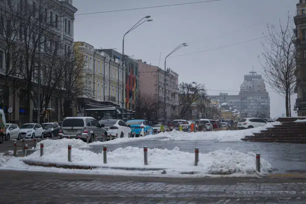 Photo of the city is hidden by white snow. people are walking outside. the architecture of the city is covered with snow