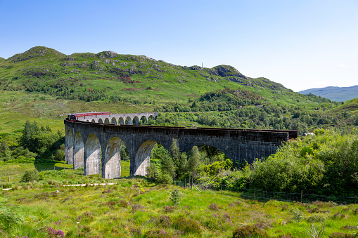 An image of the Glenfinnan Viaduct Viewpoint, capturing the iconic railway bridge as it arcs gracefully through the Scottish Highlands. Surrounded by lush greenery and rolling hills, this engineering marvel is a testament to historic construction and offers a panoramic view of the picturesque landscape.