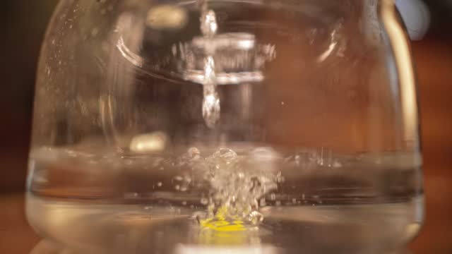 A trickle of water runs into the glass teapot, filling it. The water is bubbling.