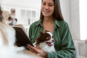 Young adult woman relaxing with a book and dogs in living room