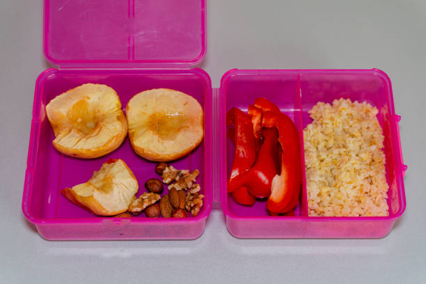 Plastic container with sandwich, vegetables and fruits on a table in a park in sunset